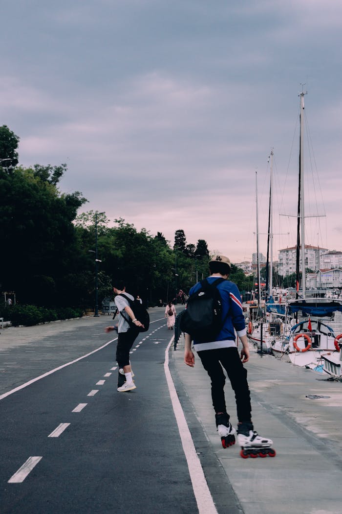 Two young adults roller skating along a city marina on a cloudy day.